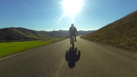 A-man-rides-a-motorized-bicycle-through-the-countryside-on-a-two-lane-road-4