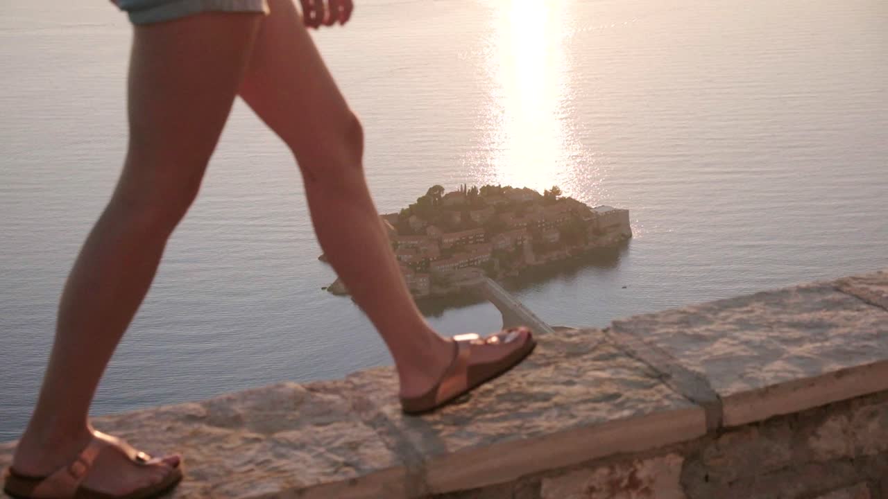 아름다운 일몰 동안 스베티 스테판 꼭대기에 있는 몬테네그로 해안선을 내려다보는 관점에서 걷는 아름다운 아가씨