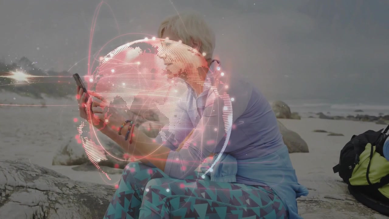 Mature woman tapping smartphone by coastal rock and visualizing glowing network globe animation