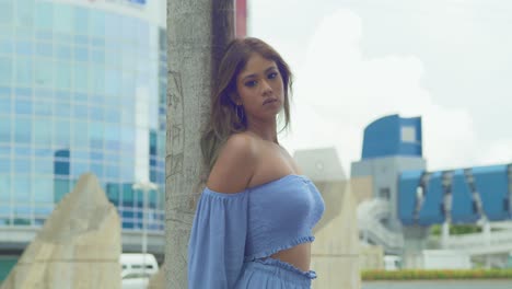 upward tilt of a young lady in a blue dress with blue skies and tall city buildings in the background