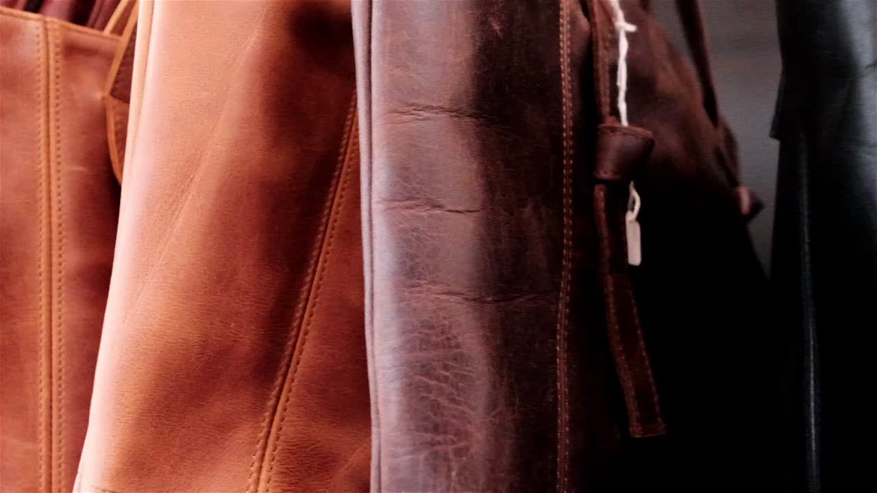 una variedad de bolsos de mano de cuero hechos a mano en diferentes colores de marrón y caramelo colgados en una tienda para la venta