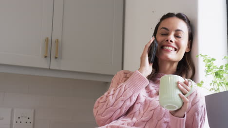 at home, woman in pink sweater talking on phone, holding coffee mug, copy space