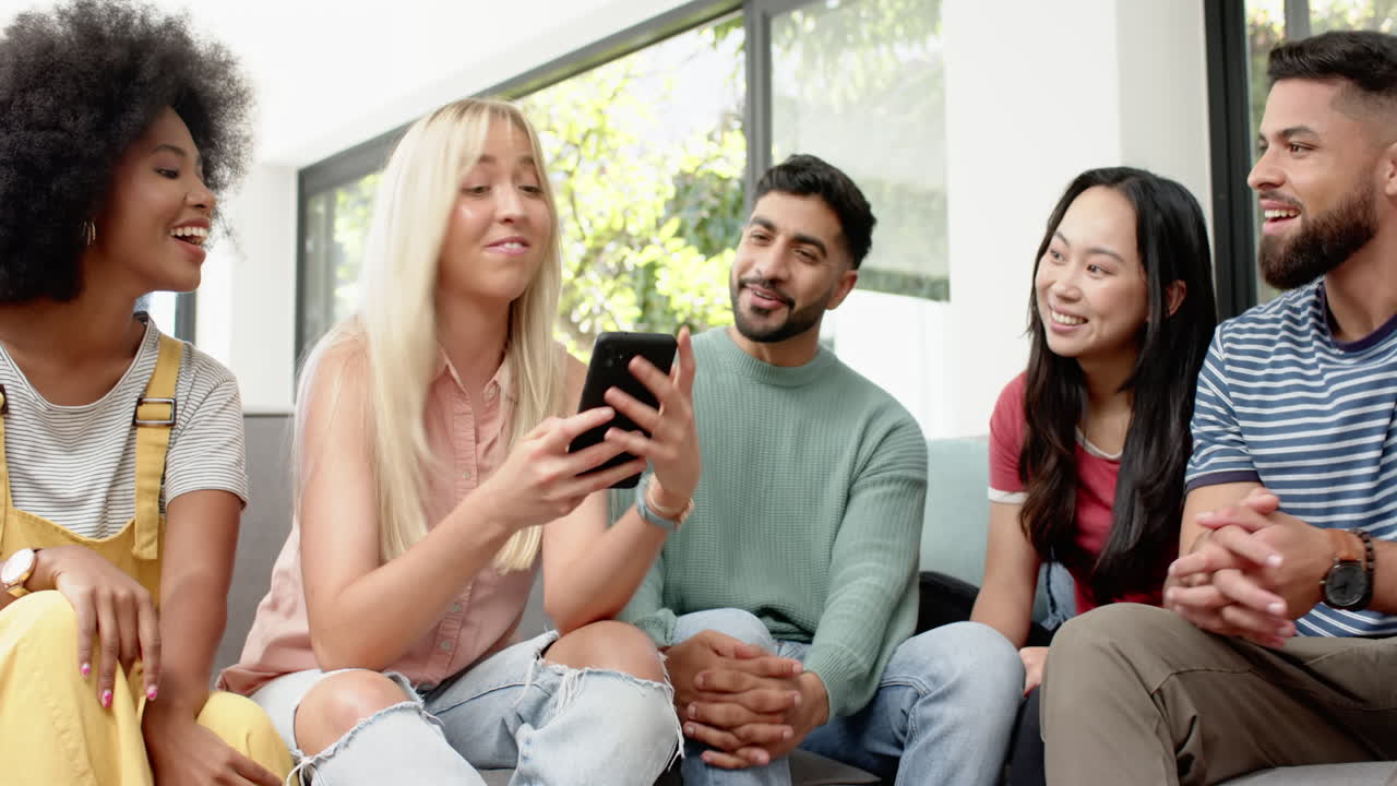 Group of young friends sitting on couch, looking at smartphone and laughing