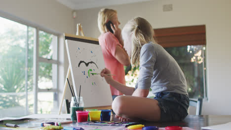 vista lateral de una niña caucásica pintando con su madre en casa