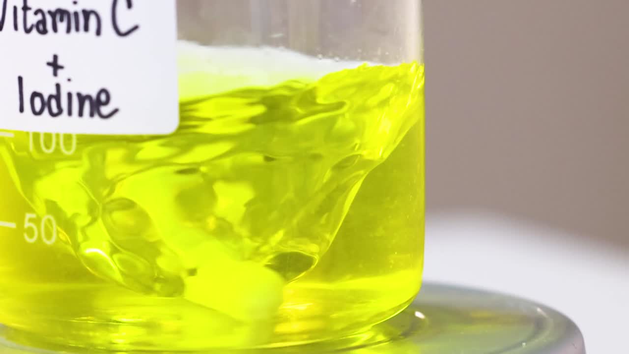 Close-up of a swirling yellow liquid in a beaker labeled 'Vitamin C + Iodine'.