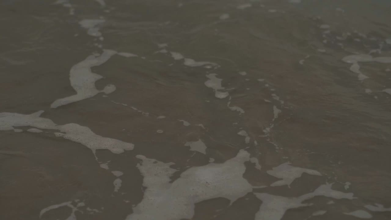 Wave passing by and crashing with white foam, cloudy horizon