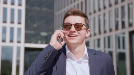 Young-man-in-sunglasses-and-suit-walks-and-talks-on-phone,-close-up