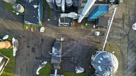 Yard-of-industrial-facility-with-asphalt-road-and-smoking-chimney,-top-down-view