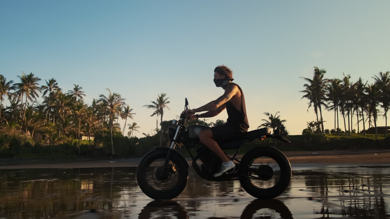 человек едет на мотоцикле на пляже при заходе солнца