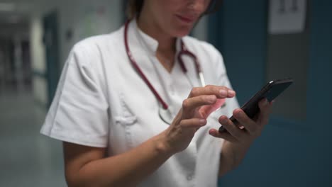 cheerful pediatrician using smartphone in hospital hallway