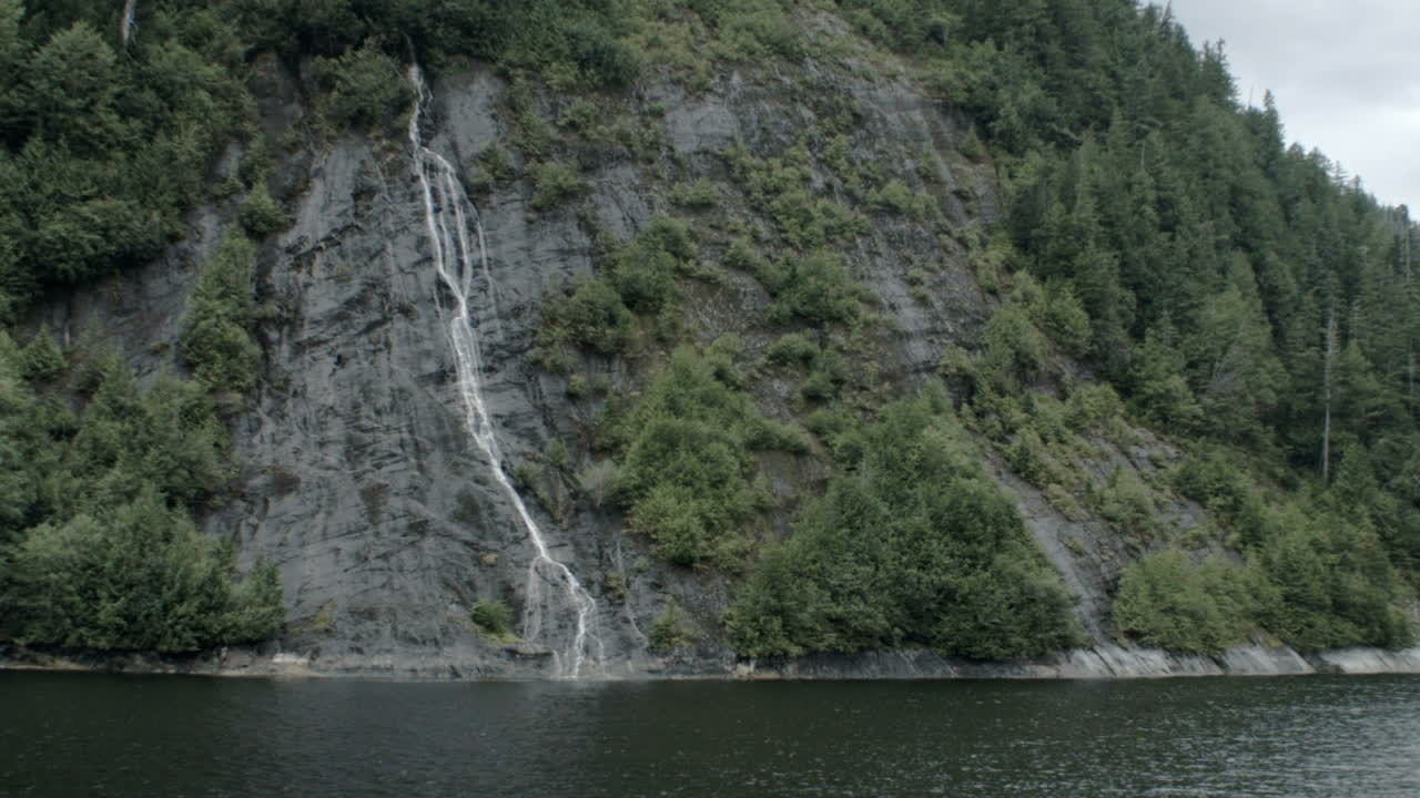Piccole cascate scendono da una montagna nell'acqua oceanica di un fiordo dell'Alaska