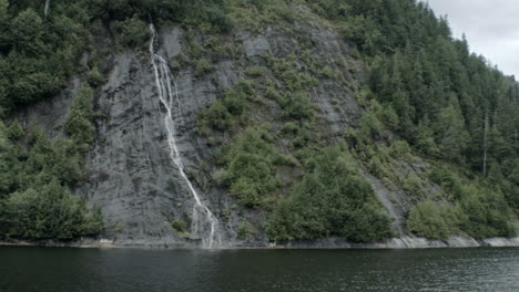 small waterfalls run down a mountain into the ocean water of an alaskan fjord