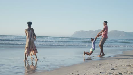 happy african american couple playing with daughter and son on sunny beach