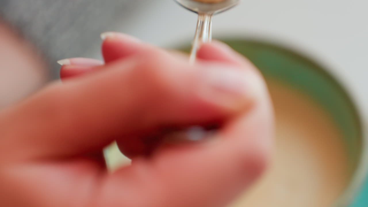 Aerial view of college student enjoying breakfast scooping from cup of hot beverage with spoon in cozy indoor setting, soft focus on creamy drink, fingers gently holding spoon with lighting