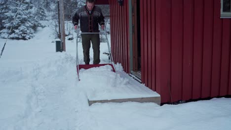 handsome man in winter clothes cleaning snow with a sled shovel at doorway and kept it inside