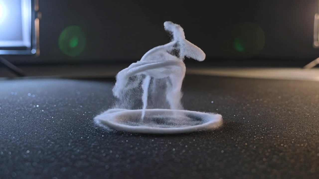 Rising white granular powder sculpting plume above circular ring on black mat, speaker vibrating