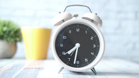 white alarm clock on a table with a yellow cup and plant