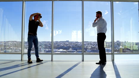 man photographing businessman in light studio. handsome man in white shirt and trousers posing on camera next to large windows in office in a bright day. profile view.