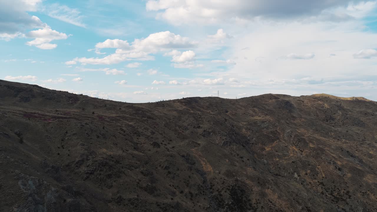 Wide aerial shot from Mount Praglia showcasing expansive mountain ridges under a vivid sky filled with scattered clouds, capturing the vastness and tranquility of the Ligurian Apennines
