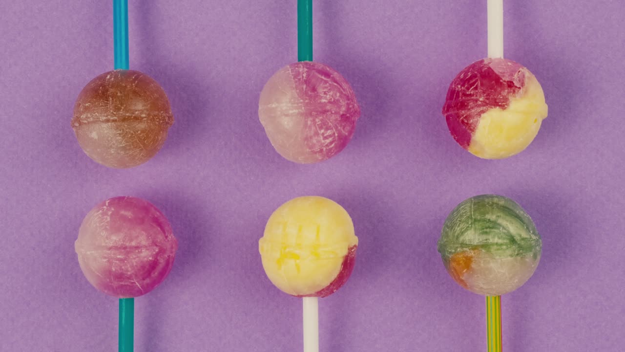 Sweet lollipops with glitter sprinkles on color purple background zoom frame. Bright texture sugar candies close up top view. Composition of favorite children&#x27;s summer sweets. Studio shot for shop, supermarket, confectionery