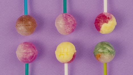 sweet lollipops with glitter sprinkles on color purple background zoom frame. bright texture sugar candies close up top view. composition of favorite children's summer sweets. studio shot for shop, supermarket, confectionery