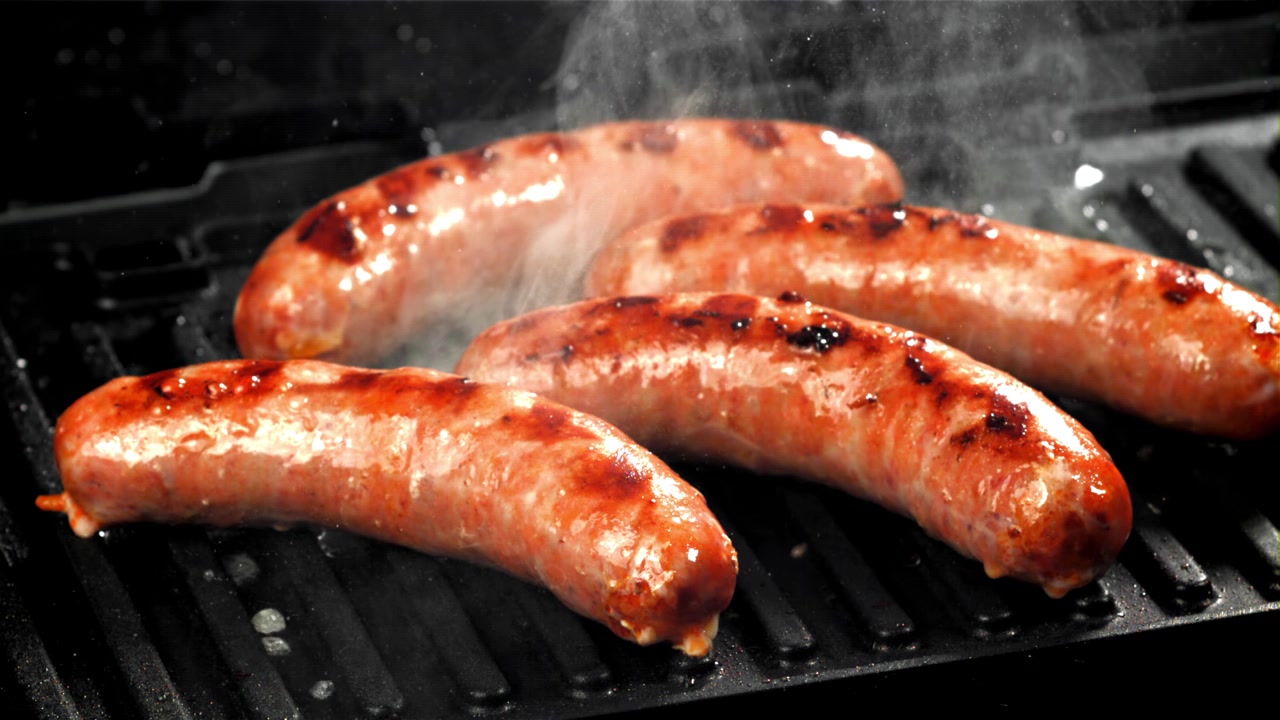 Salsicce sfrigolanti che cuociono su una griglia rovente per barbecue.