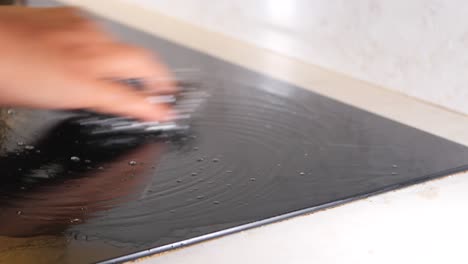 a person cleaning a black stovetop with a cleaning sponge