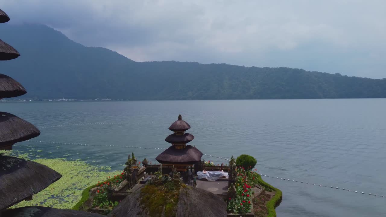 Aerial drone footage of Pura Ulun Danu Bratan, a sacred water temple on Lake Bratan in Bali. Surrounded by misty mountains and calm water, the temple appears to float peacefully in nature.