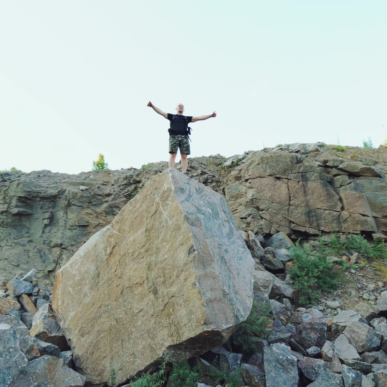 Tourist man standing on a big rock and raises his hands up on the stones background under the clear sky. Happy young hiker man tourist between the rocks outdoors.