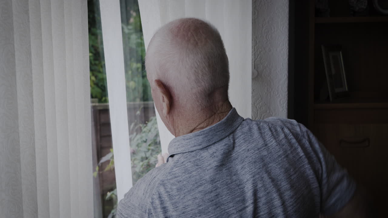 Elderly man adjusting window blinds indoors