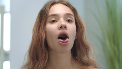 mujer joven con la boca abierta mirando la lengua y la garganta en el espejo en el baño