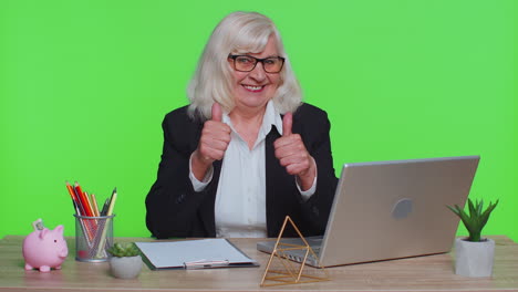 Senior-business-woman-raises-thumbs-up,-agrees,-approve,-likes-good-news-using-laptop,-green-office