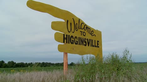 a large yellow sign points to higginsville missouri from a farm field