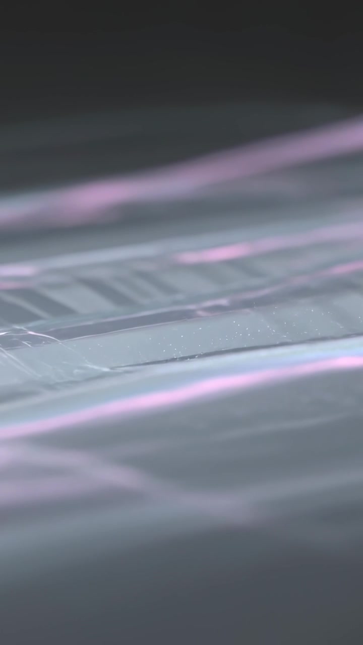Vertical video: Light sweep making rippled sheer film showing ridges and pink teal bands in studio