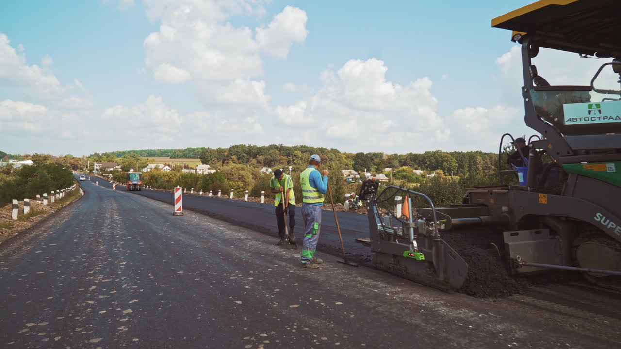 New asphalt road in the countryside. Laying of asphalt carried out by workers and pavers. Asphalt paver machine on a road construction site.