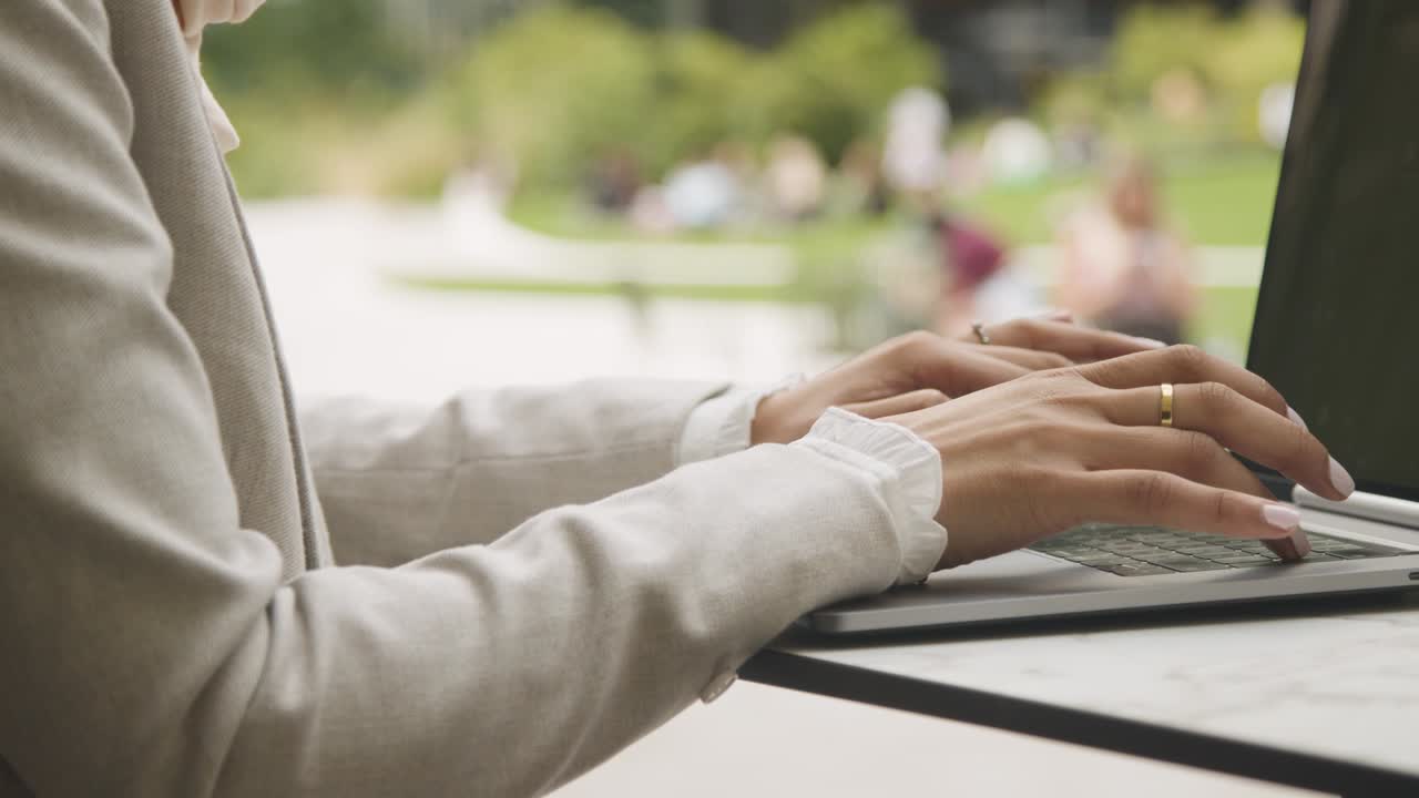 Close Up Of Businesswoman's Hands On Laptop Keyboard As She Sits Outdoors In City Gardens Working