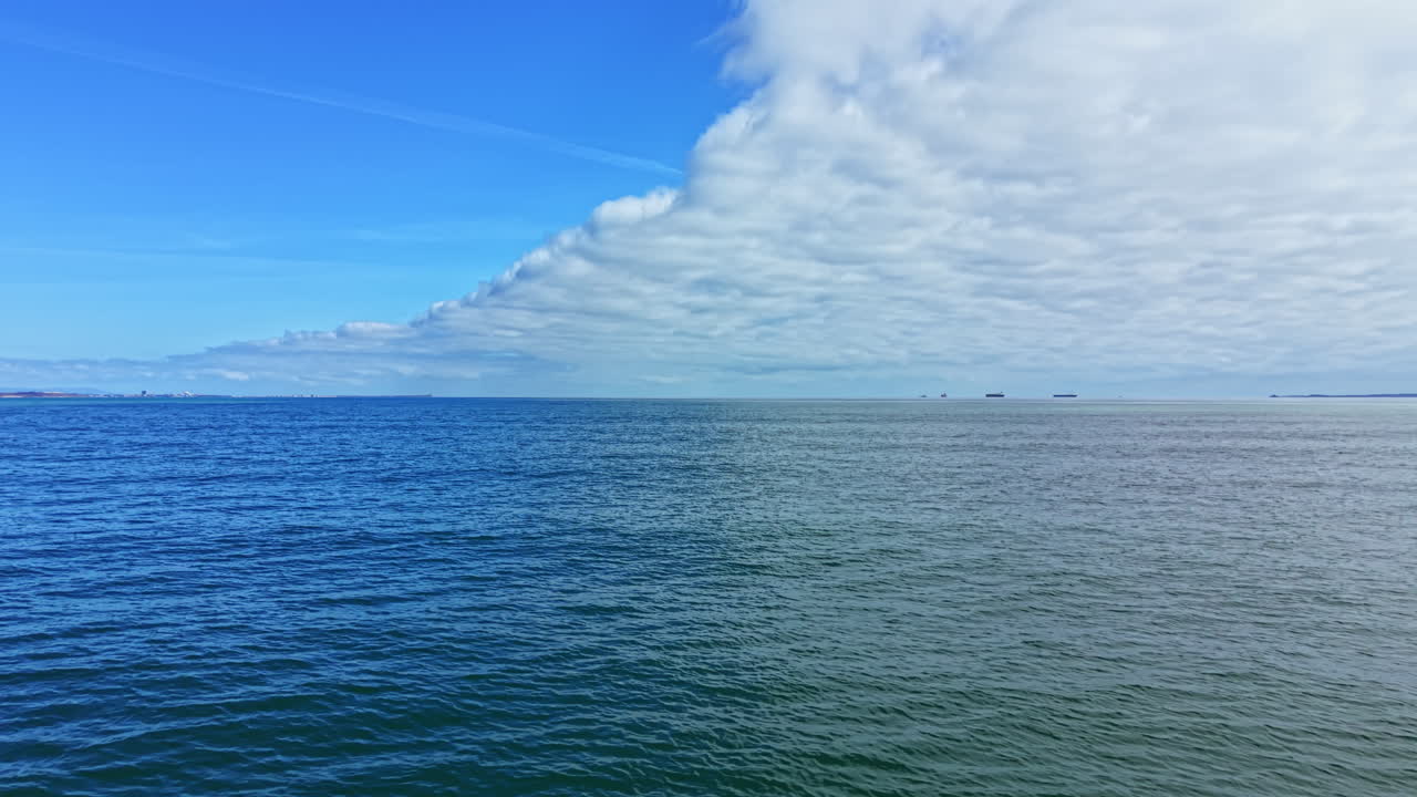 Ampia vista dell'orizzonte oceanico con navi e nuvole sotto un cielo blu durante il giorno in una località costiera