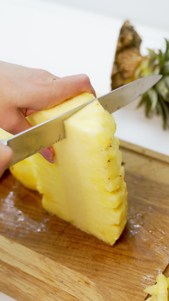 Woman cutting pineapple. Fresh pineapple on the cutting board. Hands of a female preparing exotic fruit for guests. Close-up. Vertical video
