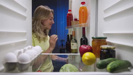woman looking inside a filled refrigerator at night