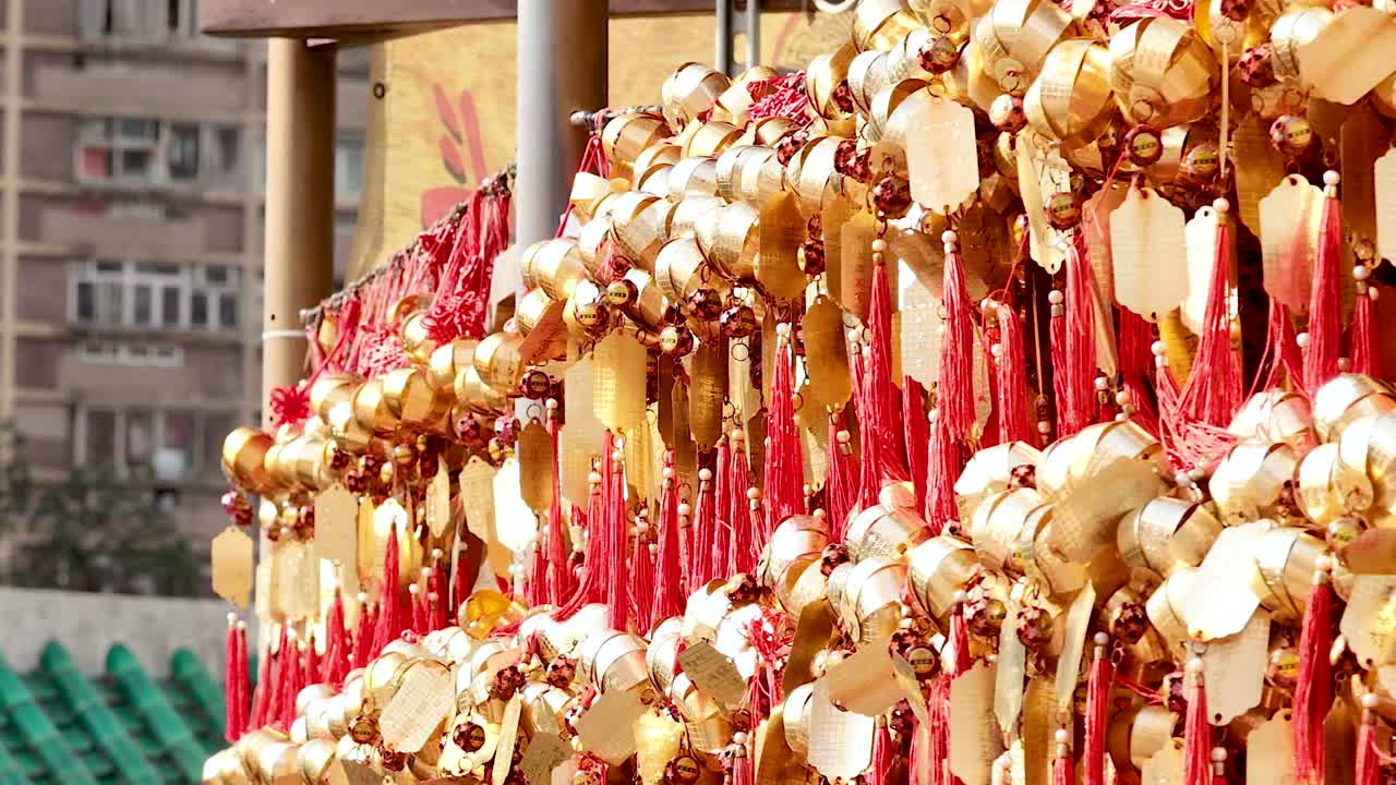 Close-up view of red and gold wishing ribbons hanging in a vibrant display against an urban backdrop.