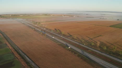 Warmes-Licht-Des-Morgenlichts-Kurz-Nach-Sonnenaufgang-Scheint-Auf-Ackerland-Und-Autobahn-Voller-Autos-Und-Lastwagen,-Wenn-Der-Tag-Beginnt