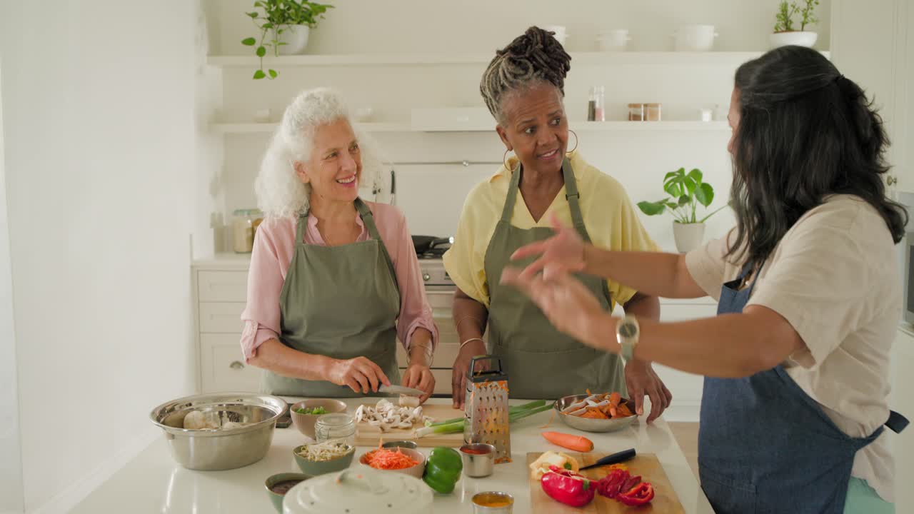 Diverse women in aprons after demo peeling, grating, checking tablet at island, prepping meal