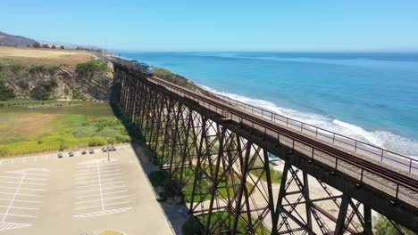 Vista-Aérea-Amtrak-Passenger-Train-Traveling-Along-The-Coast-Of-California-With-Pacific-Ocean-And-Gaviota-Trestle