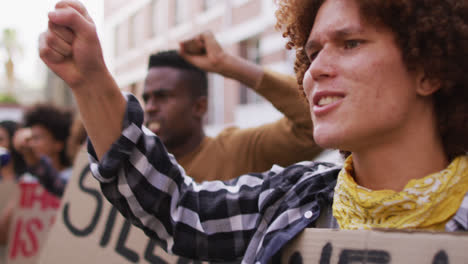 diverse group of men and women holding placards shouting raising fists during protest