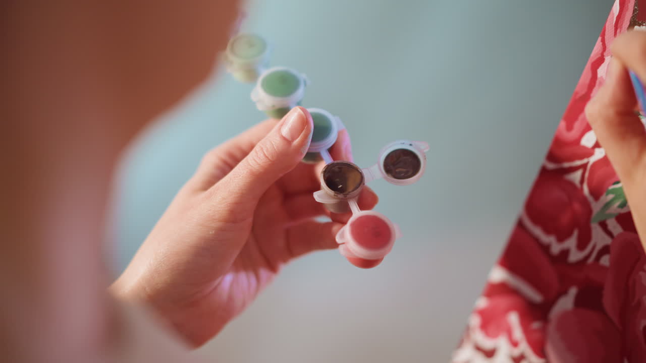 Caucasian Hands Selecting Paint From Palette, Closeup Of Fingertip And Tiny Paint Wells As Artist Prepares Brush For Fabric Detail Work, Calm Studio Moment Focused On Color Choice And Tool Handling
