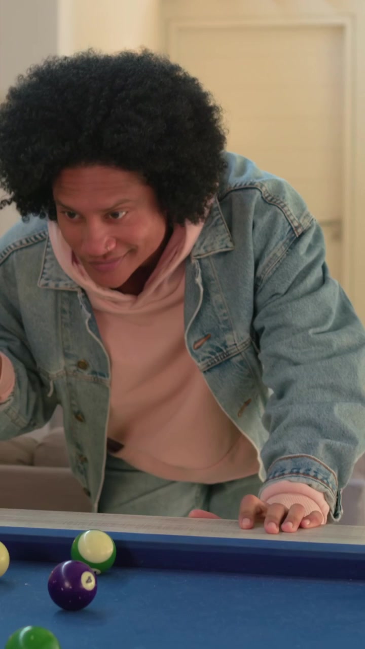 Vertical video: Placing cue on felt, man in denim jacket lining up, striking, playing pool at home