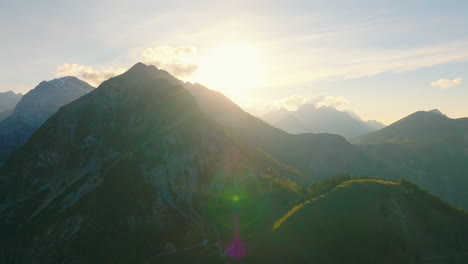 Sunrays-disappearing-behind-mountainous-woodland-peaks-of-rock-Karwendel-alpine-park-mountain-range-aerial-orbiting-view