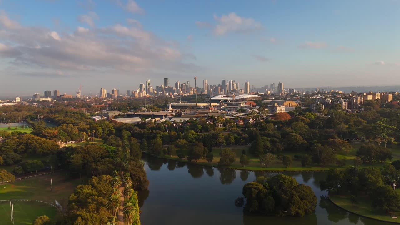 Aerial panoramic establishing of Centennial Park with skyline in background and lush trees under blue sky, Sydney NSW Australia