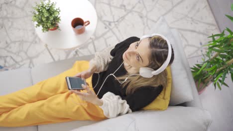 young woman listening to music in headphones relaxing on comfortable sofa with closed eyes.