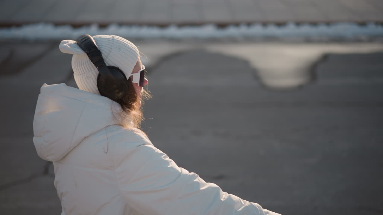 Young artist walking down tiled street wearing headphones, moving to music beat with expressive arms and joyful smile, surrounded by snowy curb and urban stair backdrop under winter sunlight